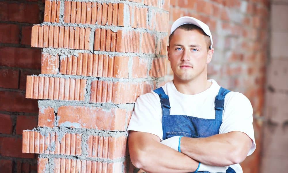 Professional masonry contractor standing beside unfinished brick wall during residential construction.