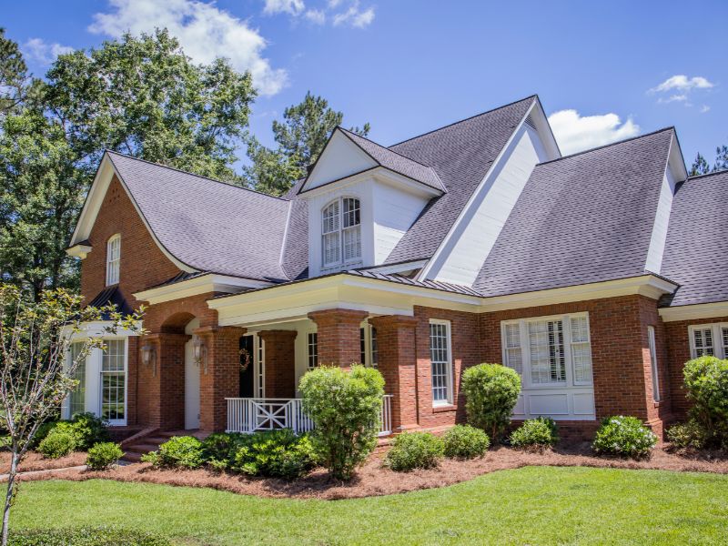 A modern two-story home featuring brick and stone masonry, surrounded by green landscaping under a clear blue sky, illustrating energy-efficient residential construction.