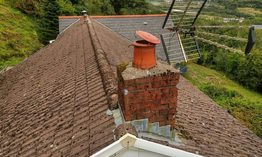 Brick fireplace chimney on a roof with worn mortar and damaged flashing, showing risk of water leaks during storms