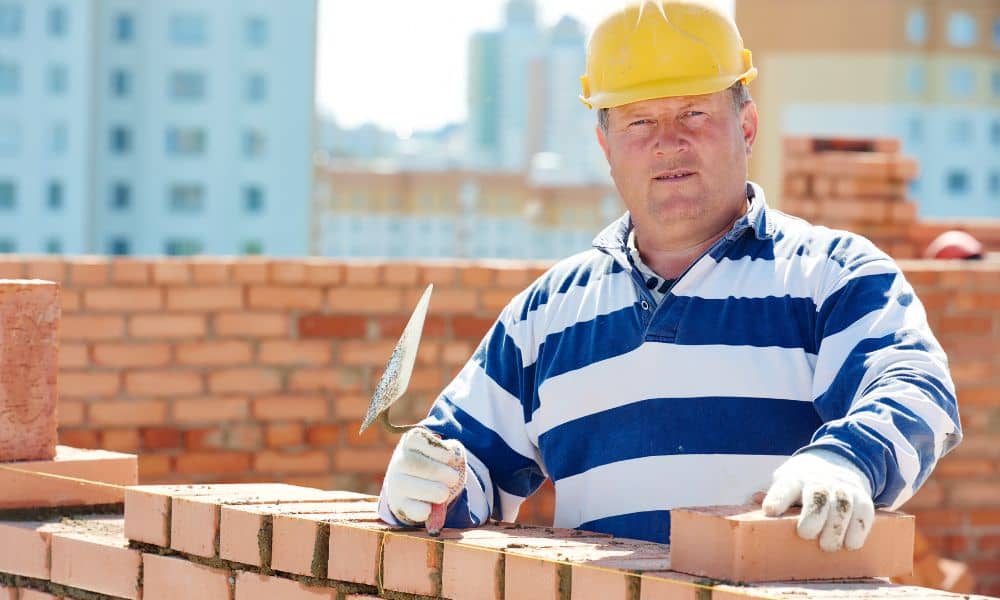 Brick mason performing brick repair on an exterior wall while preparing for weep vent installation