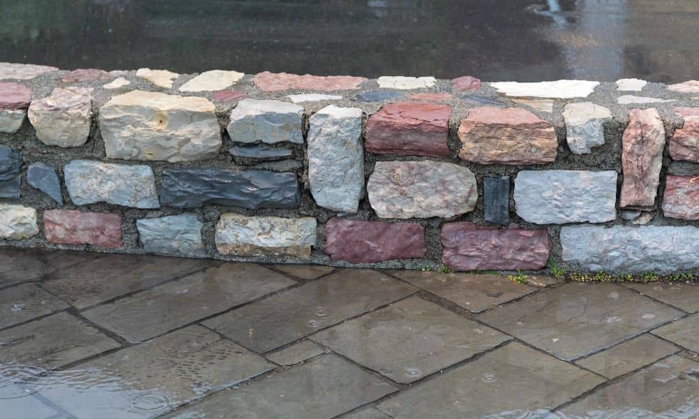 Wet stone masonry wall and pavement after a storm in North Alabama, showing water exposure and potential drainage issues.