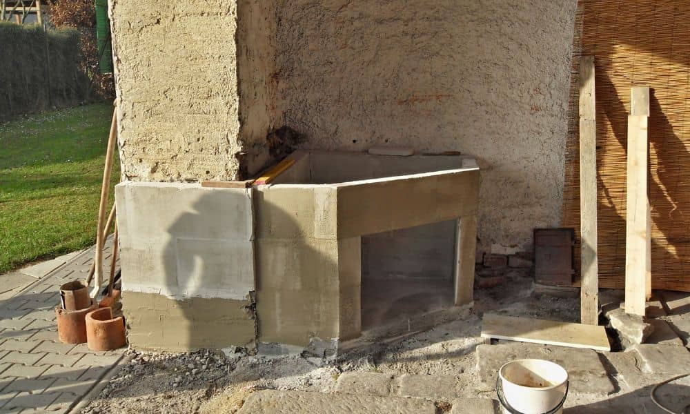 Brick mason constructing a modern outdoor fireplace on a concrete base in a backyard