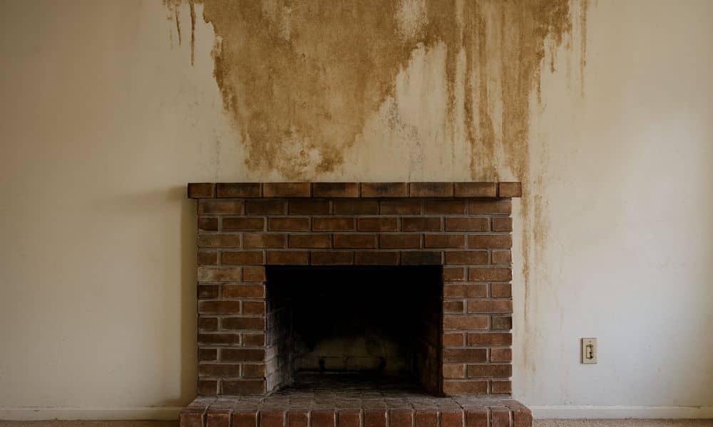 Water-stained wall above a brick fireplace showing early signs of moisture damage that often require fireplace repair
