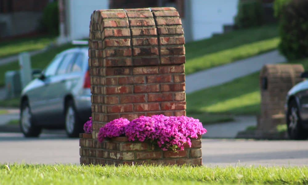 A well-built masonry mailbox with flowers around the base in a quiet neighborhood