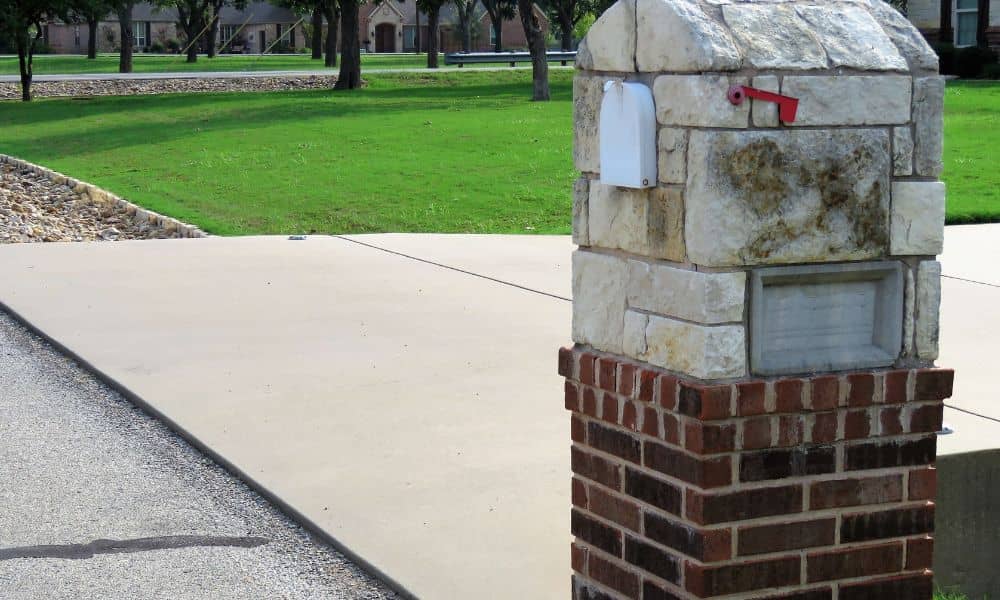 A sturdy brick mailbox built with stone and brick sitting beside a driveway, showing a secure and durable option for homeowners