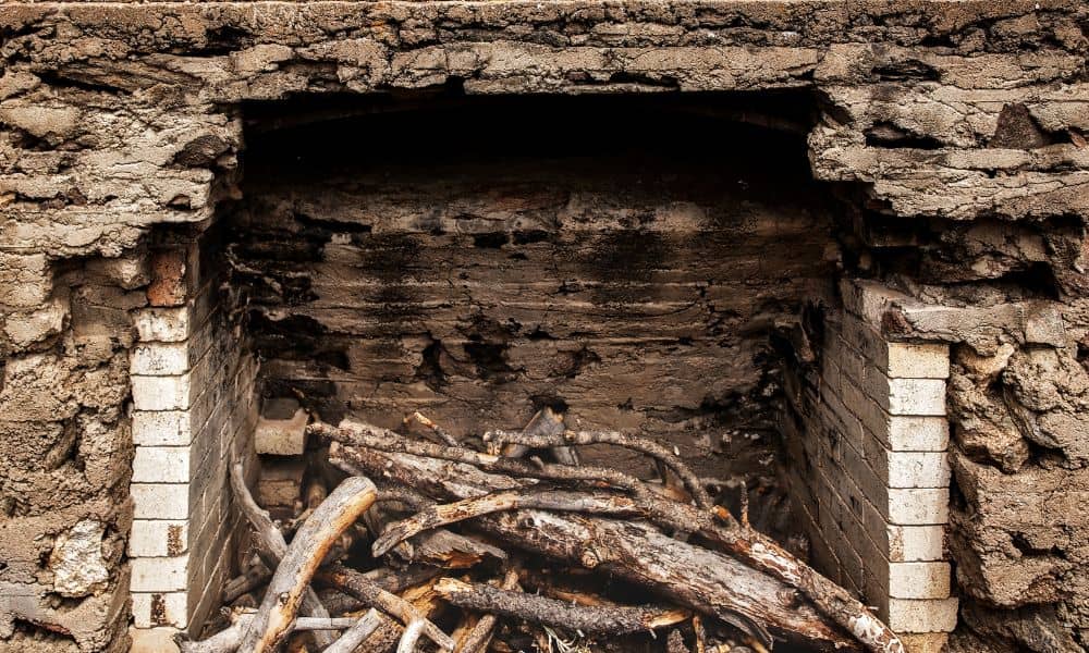A deteriorated brick fireplace showing crumbling mortar and weakened firebrick during a safety inspection