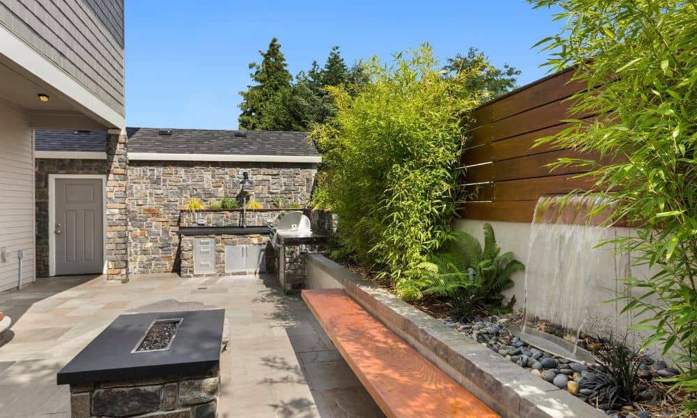 A modern outdoor kitchen with stone masonry, built-in grill, and a relaxing backyard water feature