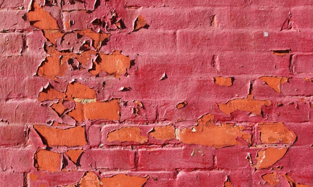 Painted brick wall with peeling paint and exposed brick caused by trapped moisture