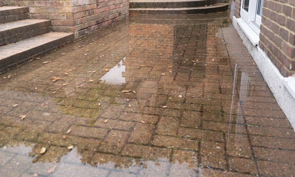 Brick patio with standing water after heavy rain showing drainage issues near the home