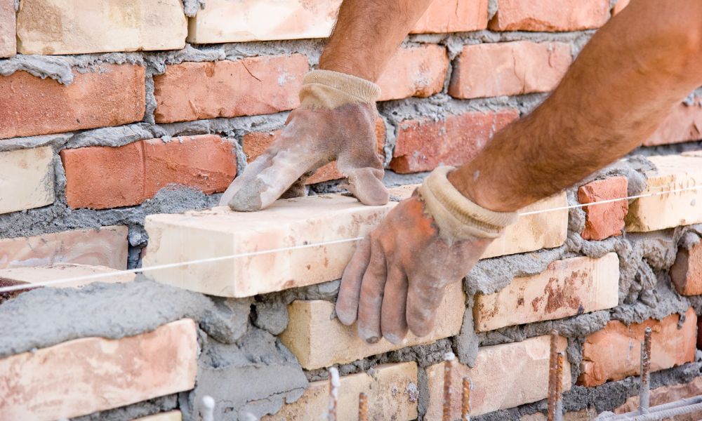 Brick mason repairing a damaged brick wall by placing new bricks and mortar to restore structural strength and appearance