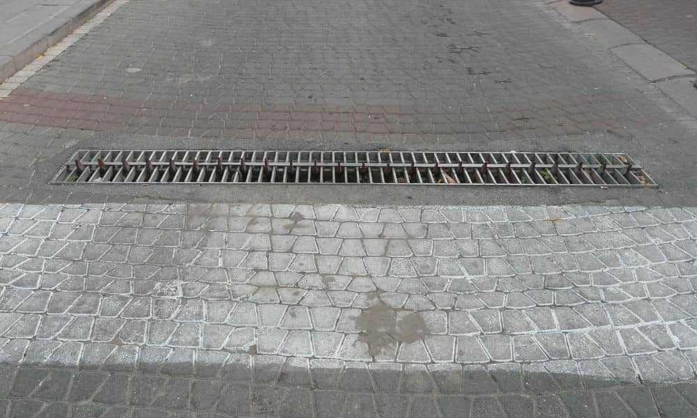 Brick pavers installed on a roadway with a drainage grate showing how proper base support helps prevent surface movement