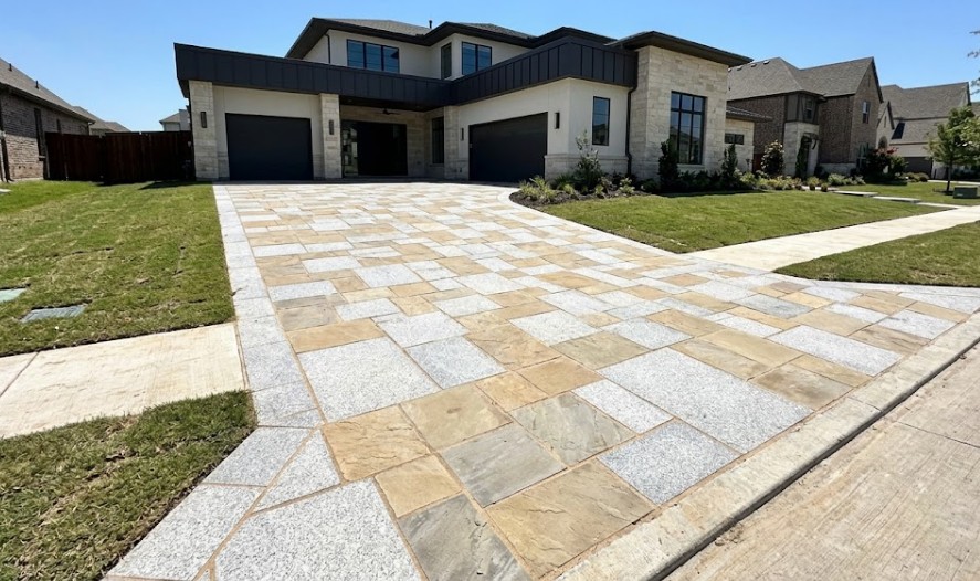 A newly installed driveway made of natural stone pavers in front of a modern Frisco home.